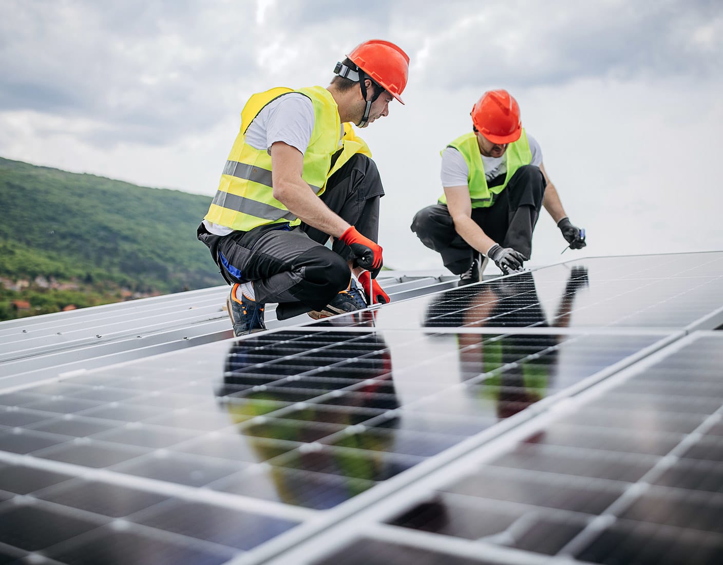 Two men in safety vests and hard hats installing solar panels on a rooftop under clear blue skies.